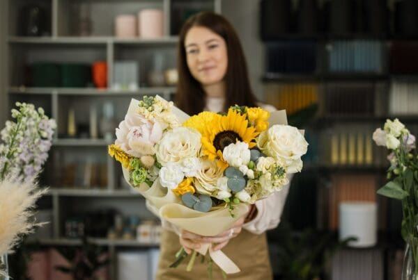 Focus on bouquet. Portrait of female florist in apron working in flower shop.